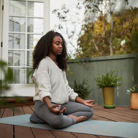 jeune femme assise dans la pose de lotus à l'extérieur sur son patio